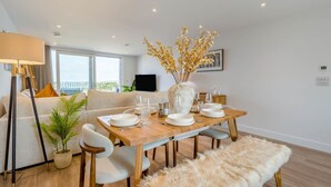 Een moderne eetruimte met een houten tafel gedekt voor vier personen, een vaas met gele bloemen en een bank op de achtergrond.