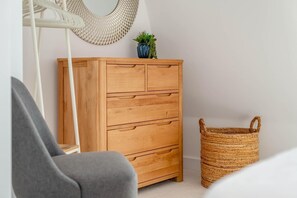 Ett träskåp med lådor, en korg av rotting, en hängstol och en liten krukväxt.