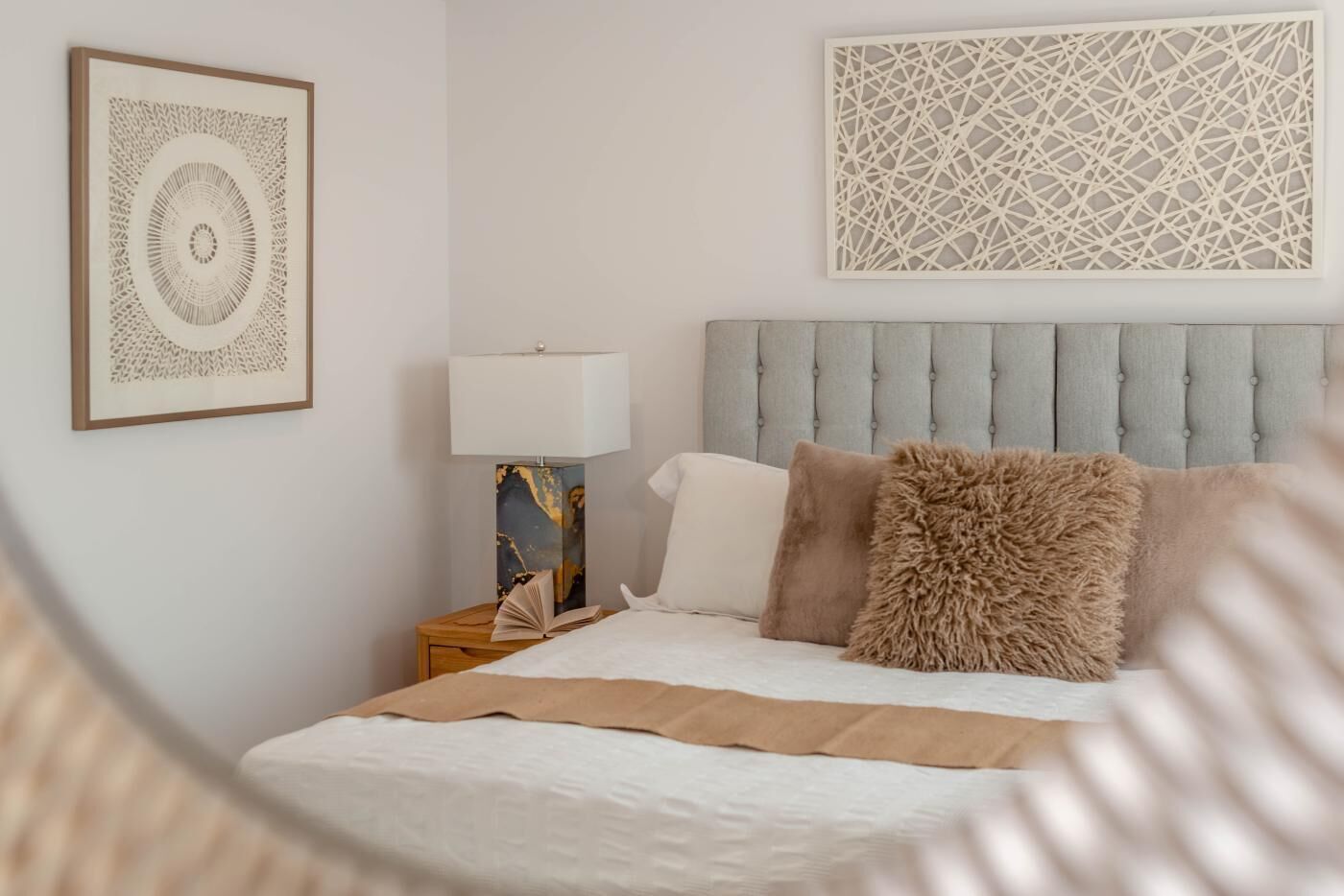 Een slaapkamer met een bed, een nachtkastje, een lamp en twee decoratieve wandobjecten.