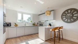 Een moderne keuken met een centraal eiland, witte kasten en een grote wandklok.