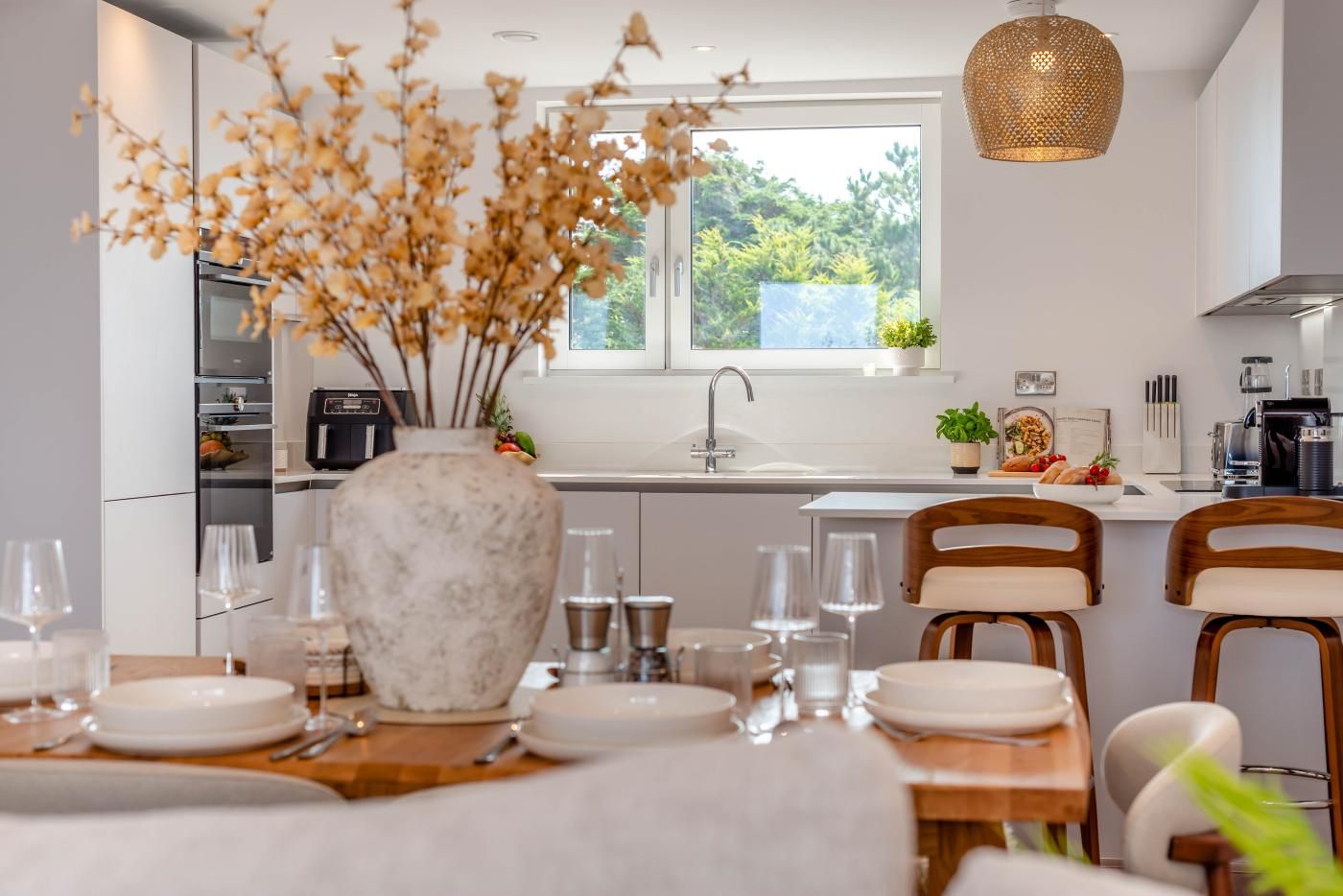 A modern kitchen with a dining area, a large window, and a vase with dried flowers.