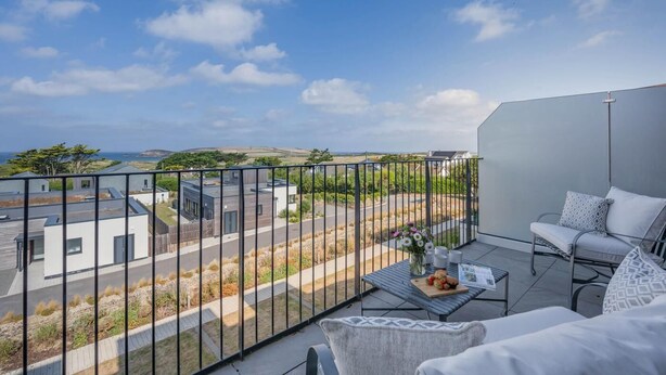 Een balkon met uitzicht op een woonwijk, een tafel met een bloemenvaas en een bank met kussens.