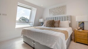 Een slaapkamer met een groot bed, een raam, een nachtkastje en een wanddecoratie.