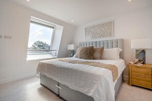 Ein Schlafzimmer mit einem großen Bett, einem Fenster, einem Nachttisch und einem an der Wand befestigten Kunstwerk.