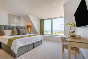 A modern bedroom with a large bed, a desk, and a view of the sea. - 3 Bed in Constantine Bay (oc-t45571) (Constantine Bay)