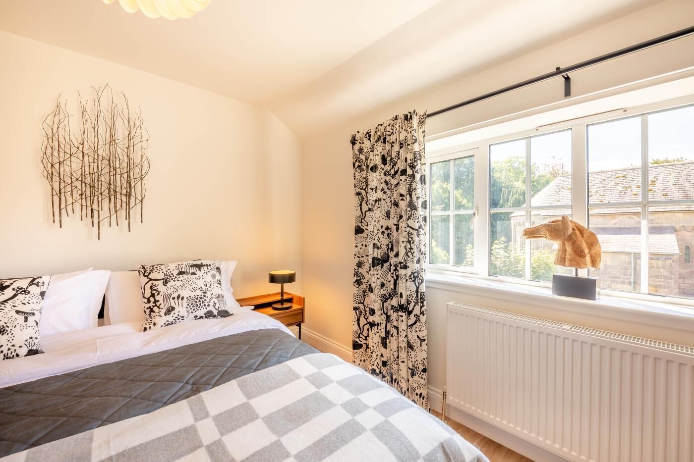 A bedroom with a bed, a nightstand, a lamp, a window with a view, and a radiator.