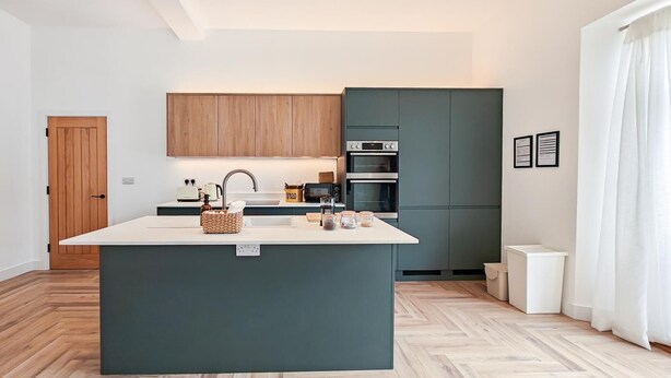 Uma cozinha moderna com uma ilha central, armários de madeira e um padrão de piso em herringbone.