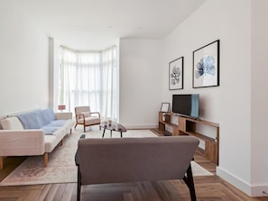 Ein modernes Wohnzimmer mit Sofa, Sessel, Couchtisch und Fernseher auf einem Holzgestell.