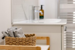 Ein Badezimmer mit einem weißen Waschbecken, einer Seifenfiole und einem gewebten Korb mit Handtüchern.