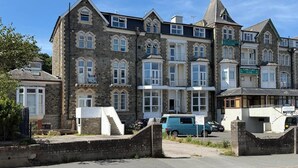 Eine Reihe von Steinhäusern mit mehreren Fenstern und Balkonen, ein blauer Transporter vor der Fassade und ein Schild, das ein Hotel anzeigt.
