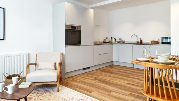 Eine moderne Küche mit weißen Schränken, einem eingebauten Backofen und einem Essbereich mit Holztisch und Stühlen.