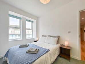Ein Schlafzimmer mit einem Bett, zwei Nachttischen, einem Fenster und einer Tür.