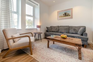 A living room with a sofa, a chair, a coffee table with fruit, and a painting on the wall. - 2 Bed in Ilfracombe (oc-b45844) (Ilfracombe)