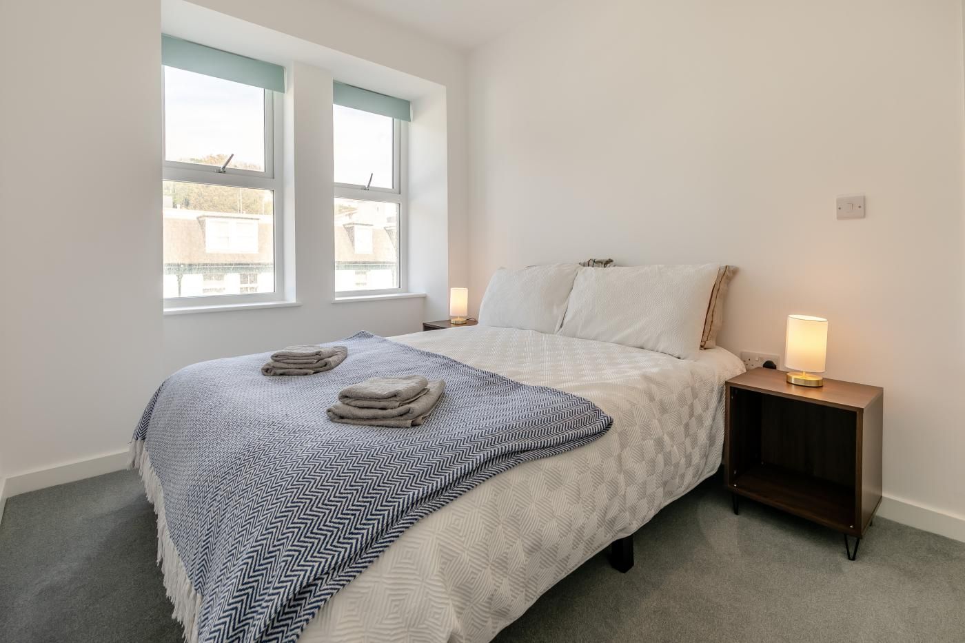 Ein Schlafzimmer mit einem Bett, zwei Nachttischlampen, einem Fenster und einem Nachttisch.