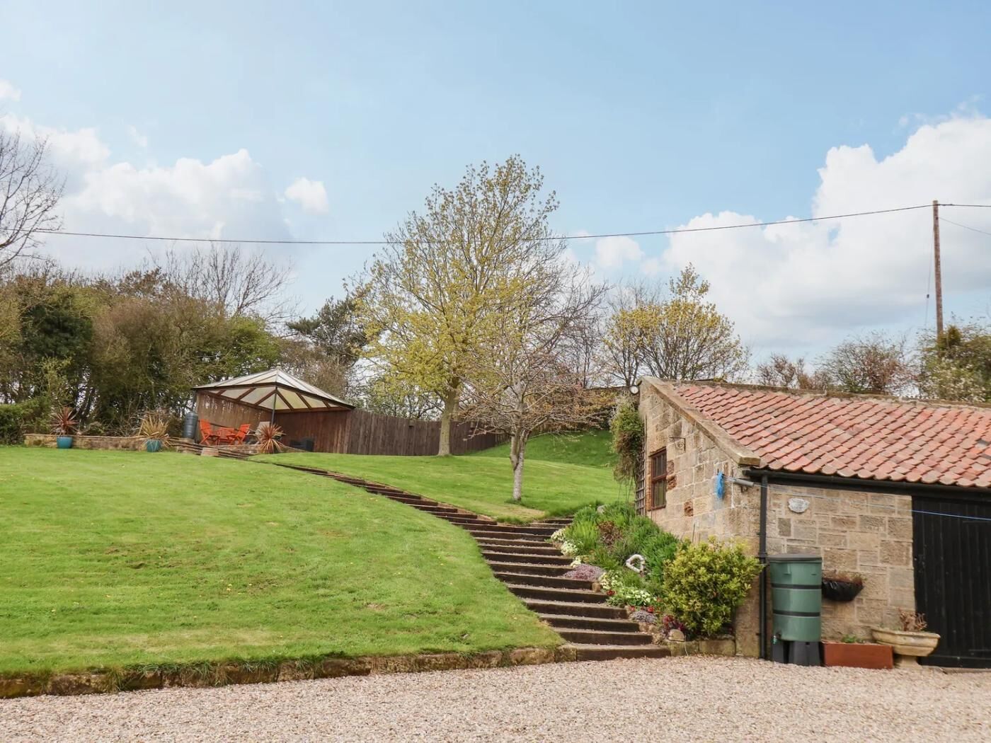 A rural property with a stone building, a wooden shed, a well-maintained lawn, and a gravel driveway.
