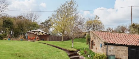 A rural property with a stone building, a wooden shed, a well-maintained lawn, and a gravel driveway.