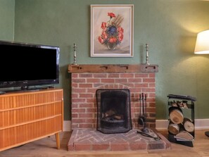 Ein Wohnzimmer mit Kamin aus Ziegelsteinen, einem Fernseher auf einem Holzbalken und einem Holzscheckenständer.