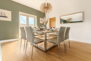 A dining area with a round table, grey chairs, and a modern chandelier. - 4 Bed in Marhamchurch (oc-h45831) (Hobbacott)