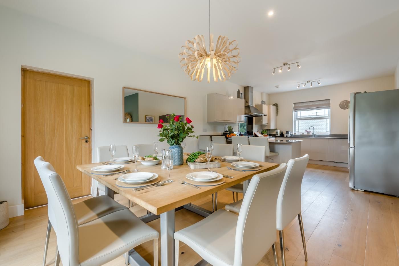 A modern kitchen with a dining area, wooden flooring, and white furniture.
