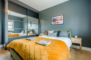 A modern bedroom with a large bed, a green headboard, and a bedside table with a lamp. - 4 Bed in Marhamchurch (oc-h45831) (Hobbacott)