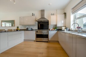 A modern kitchen with a central stove, white cabinets, and a window providing natural light. - 4 Bed in Marhamchurch (oc-h45831) (Hobbacott)