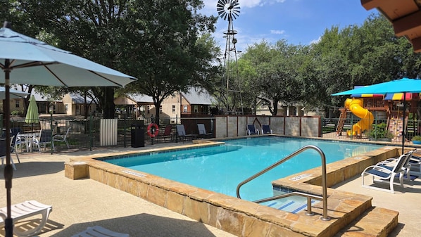 Una piscina con un puesto de salvavidas, sillas de descanso y un molino de viento al fondo.