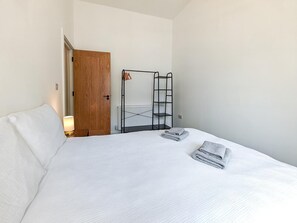 A hotel room with a bed, a wooden door, a radiator, and a metal shelf unit. - 2 Bed in Ilfracombe (oc-b45842) (Ilfracombe)