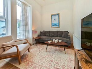 A living room with a sofa, a coffee table, a lamp, and a poster on the wall. - 2 Bed in Ilfracombe (oc-b45842) (Ilfracombe)