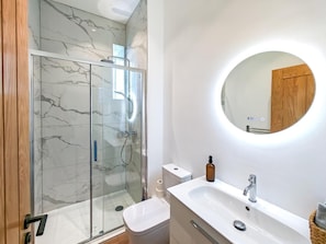 A modern bathroom with a glass-enclosed shower, a round mirror, and a white sink with a wooden door. - 2 Bed in Ilfracombe (oc-b45842) (Ilfracombe)
