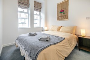 A neatly made bed with a patterned blanket and folded towels, a bedside lamp, and a wall-mounted sign indicating the room is a product of Vietnam. - 2 Bed in Ilfracombe (oc-b45842) (Ilfracombe)