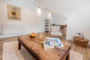 Ein modernes Wohnzimmer mit einem Holztisch, einer Obstschale, einem Puzzlespiel und einem Korbwägelchen.