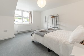 Une chambre à coucher avec un lit, un radiateur, une fenêtre et une étagère fixée au mur.