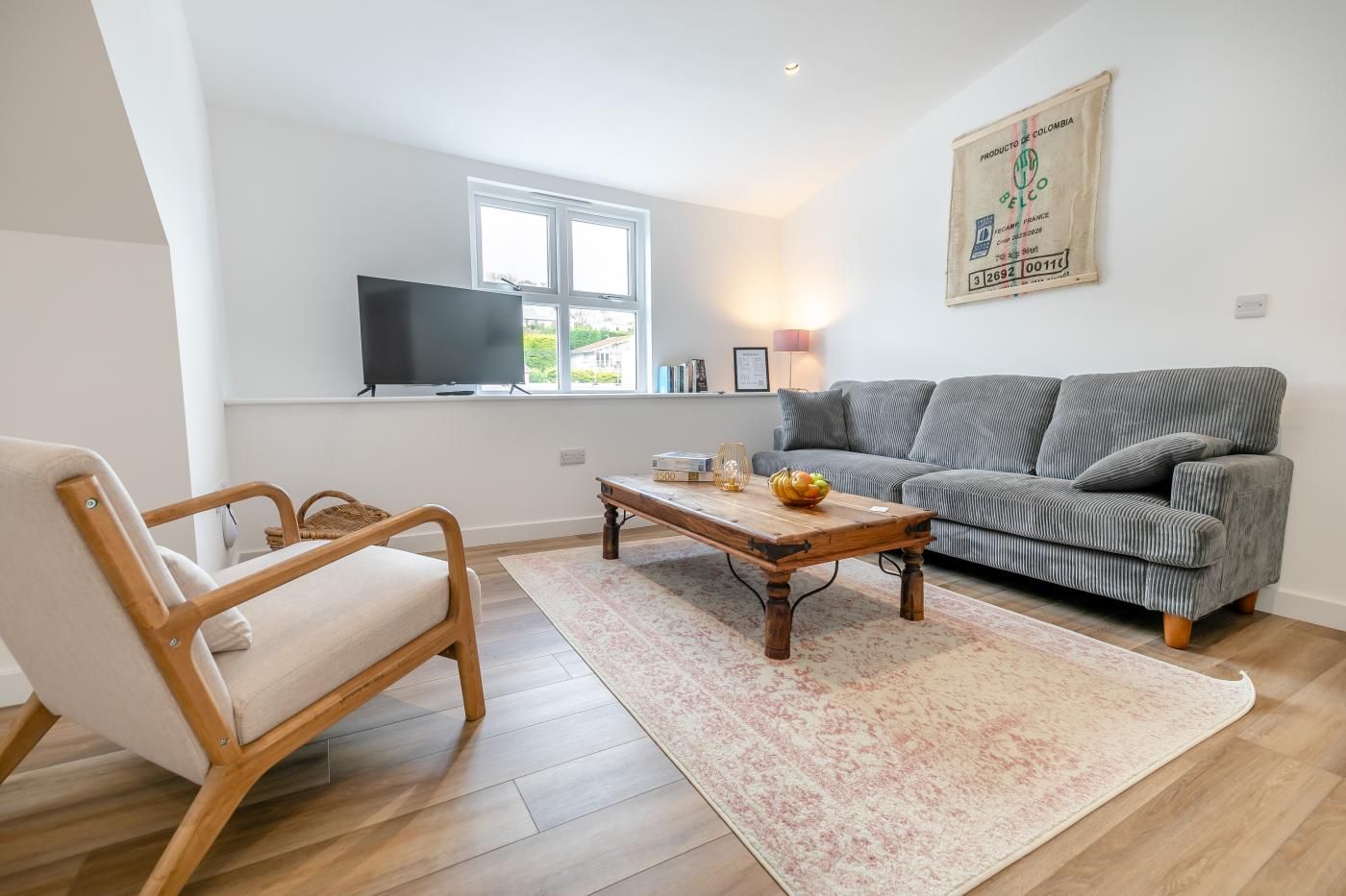 Ein Wohnzimmer mit einer Couch, einem Holztisch, einem Korbstuhl, einem flachbildfernseher an der Wand und einem Fenster mit Blick.