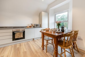 Eine moderne Küche mit weißen Schränken, einem Holztisch und einem großen Fenster.