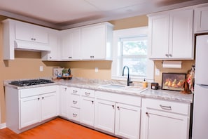 A kitchen with white cabinets, a granite countertop, a stainless steel range, and a window with a view. - Cozy 2-bedroom house in Cotter, walking distance to shopping, river, and food. (Cotter)