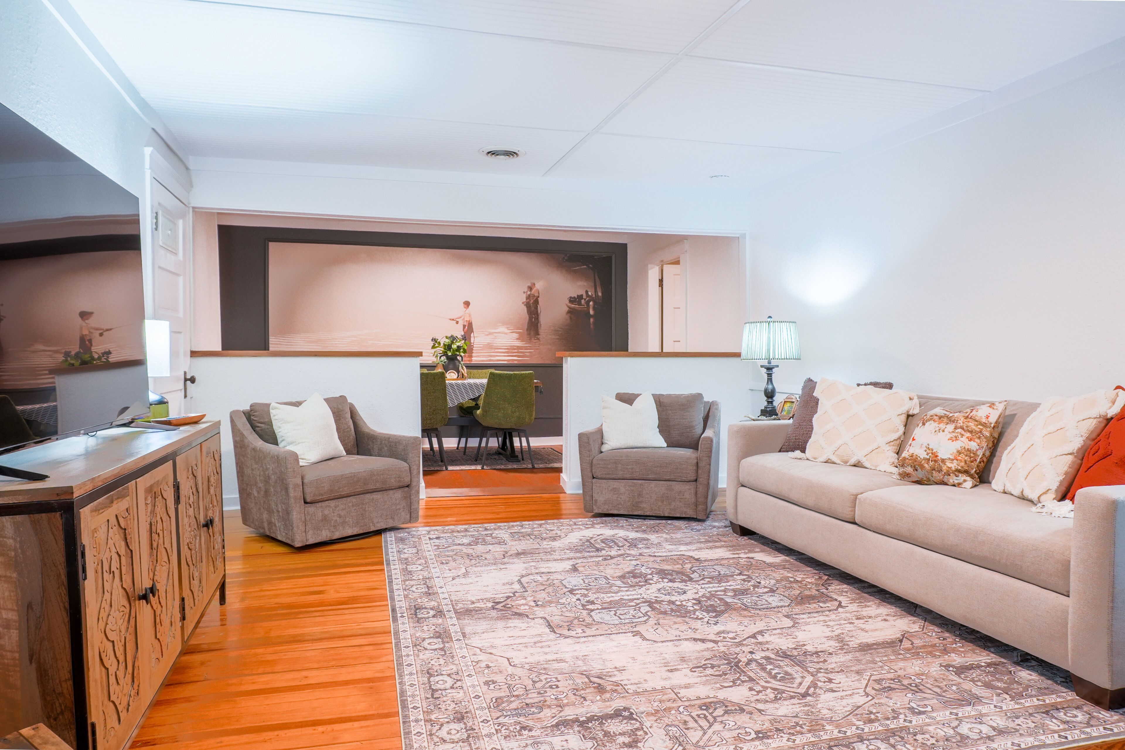 A living room with a sofa, two armchairs, a coffee table, a TV, a dining table with chairs, and a patterned rug.