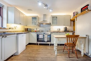 A kitchen with white cabinets, a central stove, a wooden dining table, and a chair. - 3 Bed in Stoborough (oc-c44898) (Stoborough)