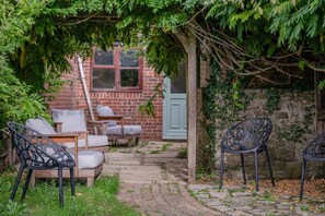 A brick building with a wooden door, a stone wall, and a garden area with outdoor furniture. - 3 Bed in Stoborough (oc-c44898) (Stoborough)