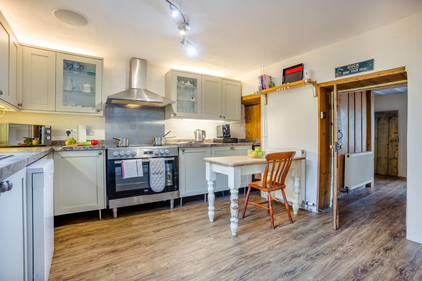 A kitchen with a stove, oven, and cabinets. There is a table with a chair and a sign on the wall.