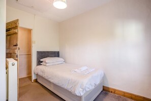 Ein Einzelbett mit weißer Bettwäsche in einem Zimmer mit Holztür und weißer Wand.
