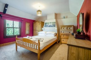 A bedroom with a wooden bed, a dresser, a mirror, and a window with a view of greenery. - 3 Bed in Stoborough (oc-c44898) (Stoborough)