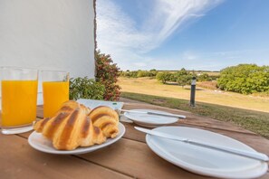 Een ontbijttafel met croissants, sapglazen en uitzicht op een grasveld.