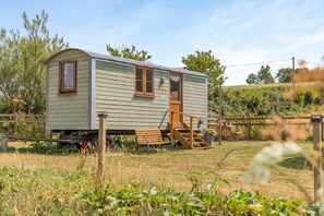 A small, single-story mobile home with a wooden door and window, a ramp leading to the entrance, and a fenced yard.