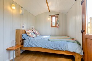 A small, cozy bedroom with a single bed, wooden headboard, and a window with curtains.