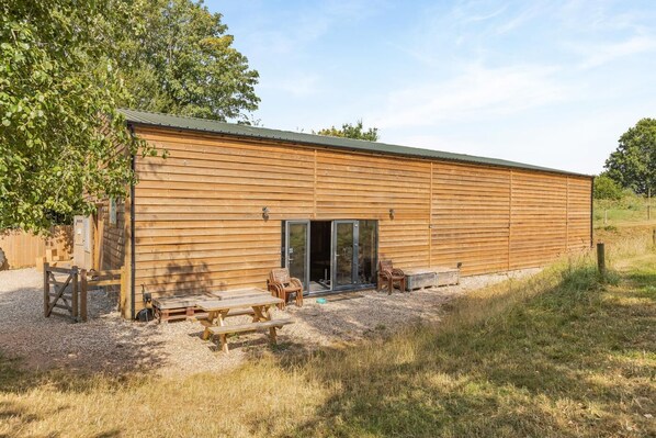 A wooden cabin with a sliding glass door entrance, a picnic table, and outdoor seating.