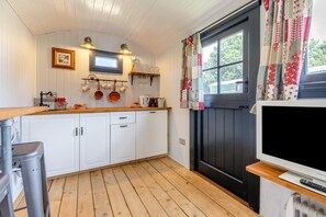 A kitchen with white cabinets, wooden countertops, a black door, and a TV on a stand. - 1 Bed in Washfield (oc-s45538) (Tiverton)