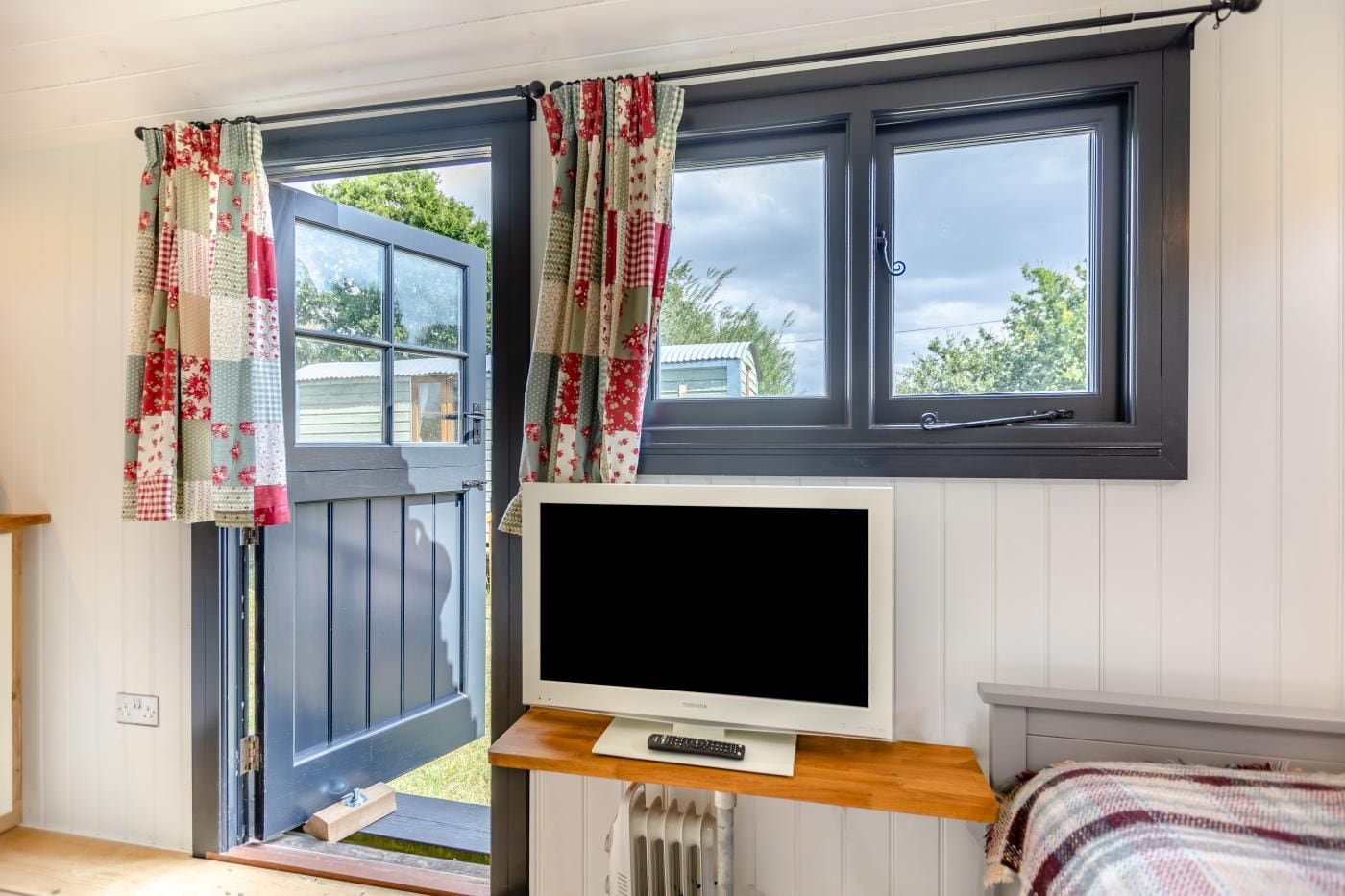 Une pièce avec un téléviseur posé sur un meuble en bois, une fenêtre avec des rideaux et une vue sur l’extérieur.