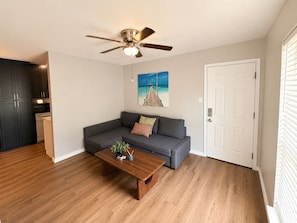 A living room with a grey sofa, a wooden coffee table, a ceiling fan, and a painting of a beach scene. - Lovely 2-bedroom apartment with AC in peaceful Arlington (Arlington)