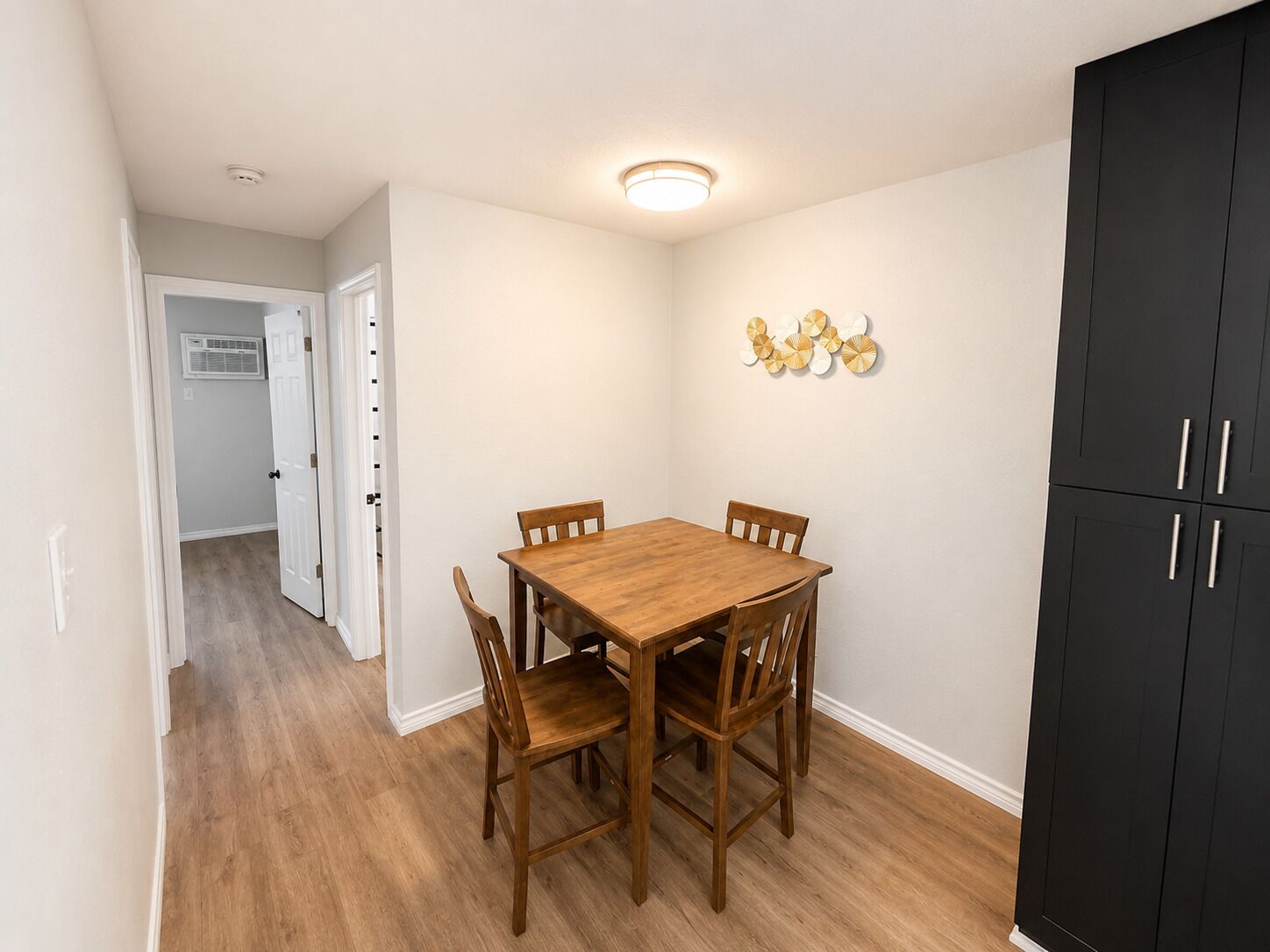 A dining area with a wooden table and chairs, a black cabinet, and a ceiling light fixture.