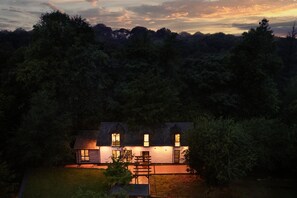 Una casa de dos pisos con un porche iluminado y un espacio de terraza visible.